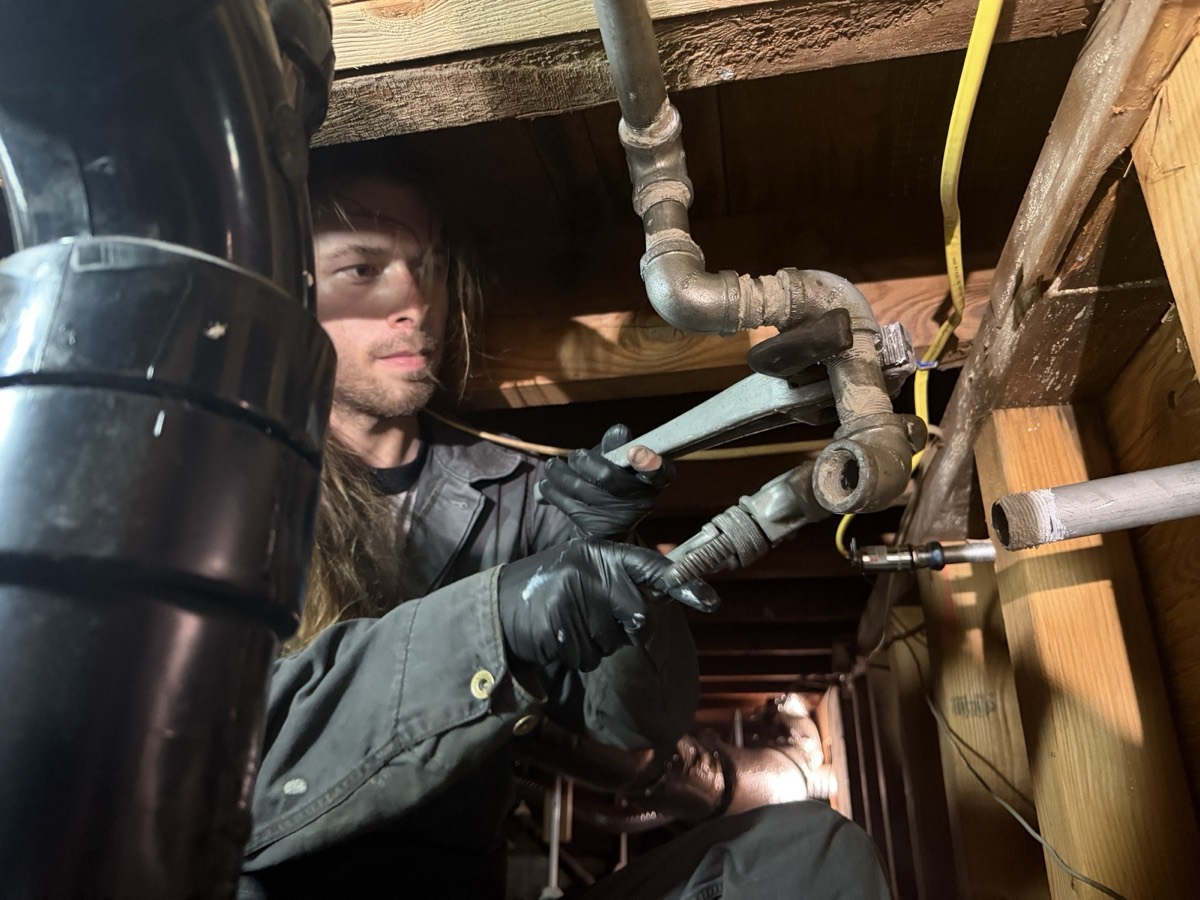 Zach working on galvanized pipe fittings in a crawlspace under a house